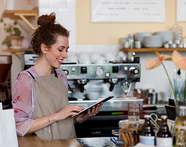 Frau in einem Kaffeehaus nutzt Tablet um sich ihren Firmenbuchauszug von FirmenABC zu holen.