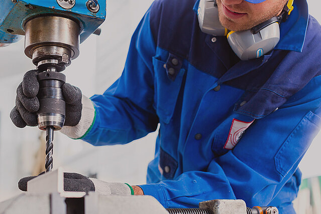 Ein junger Handwerker stellt einen Standbohrer ein um Metall so präzise wie möglich zu bearbeiten.