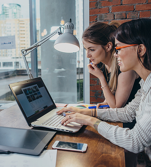 Zwei Frauen arbeiten am Design einer Website und nutzen einen Laptop um Bilder zu suchen.