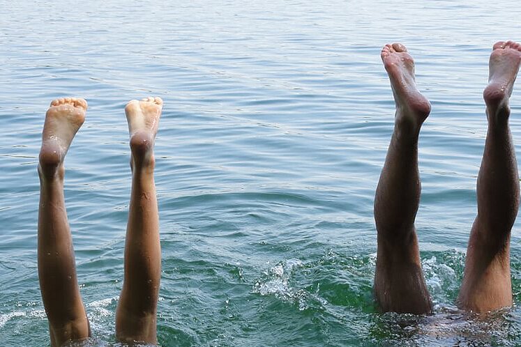 Ein Paar macht einen Kopfstand im Wasser und streckt die Füße in die Luft.