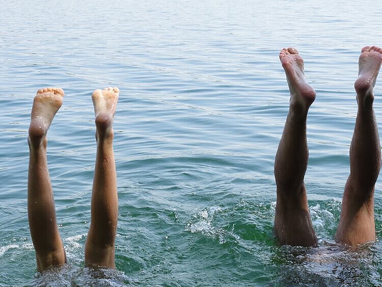 Ein Paar macht einen Kopfstand im Wasser und streckt die Füße in die Luft.