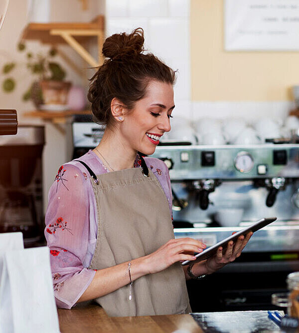 Frau in einem Kaffeehaus nutzt Tablet um sich ihren Firmenbuchauszug von FirmenABC zu holen.