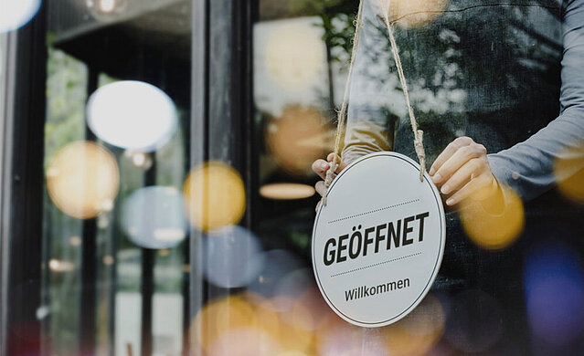 "Geöffnet"-Schild an der Glastür eines Coffee-Shops. Durch Google Werbung bekommt das Unternehmen mehr Sichtbarkeit.