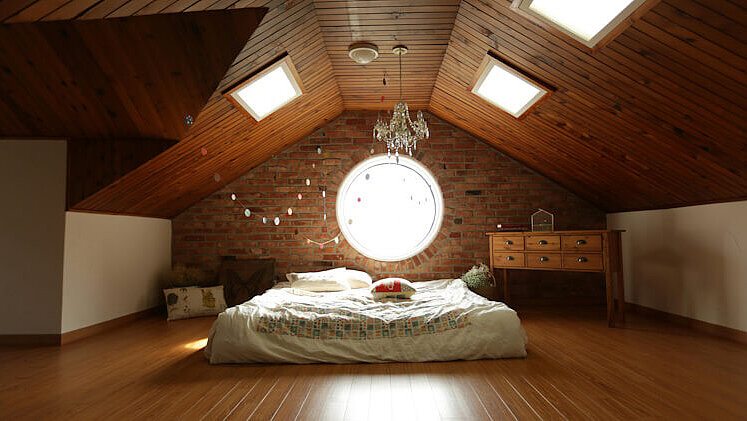 Ein warm eingerichtetes Dachgeschosszimmer mit Holzdecke. 