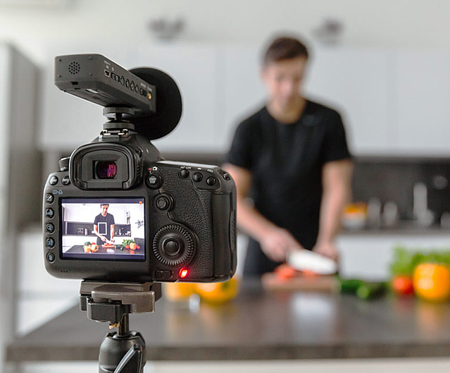 Filmdreh für ein gastronomisches Unternehmen. Kamera filmt Mann beim Schneiden von Gemüse.