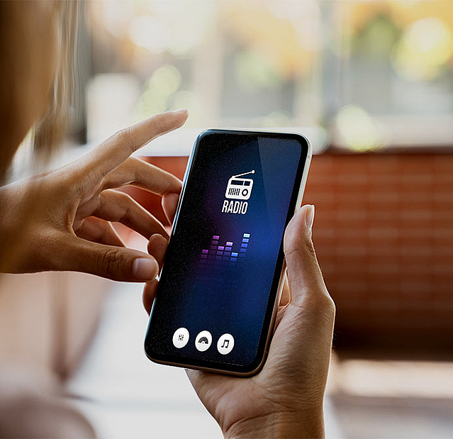 Frau sucht am Smartphone nach einem Digitalradiosender. Sie hört Radiowerbung von FirmenABC.