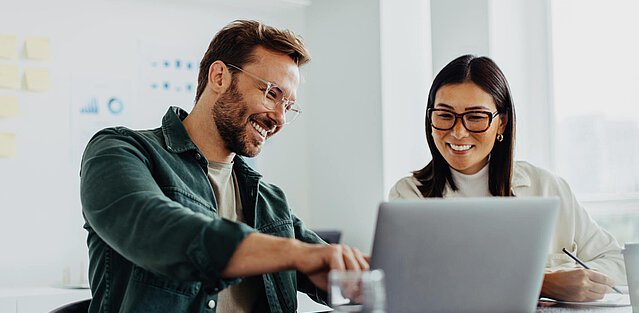 Zwei Unternehmer verwenden einen Laptop im Büro um Firmen zu suchen.