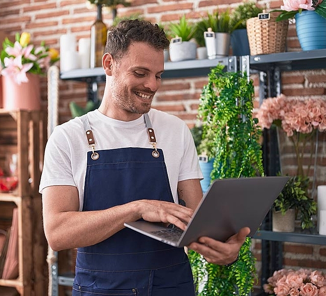 Florist schaut lächelnd in den Laptop, weil er seinen Eintrag auf FirmenABC sieht. 