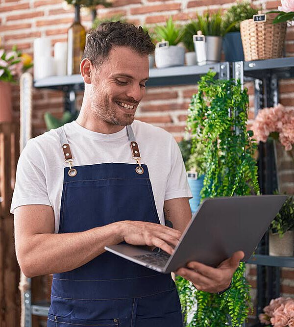 Florist schaut lächelnd in den Laptop, weil er seinen Eintrag auf FirmenABC sieht. 