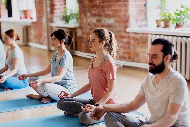 Eine Gruppe von Menschen macht Yoga in einem Fitnessstudio, dass sie auf FirmenABC gefunden haben.